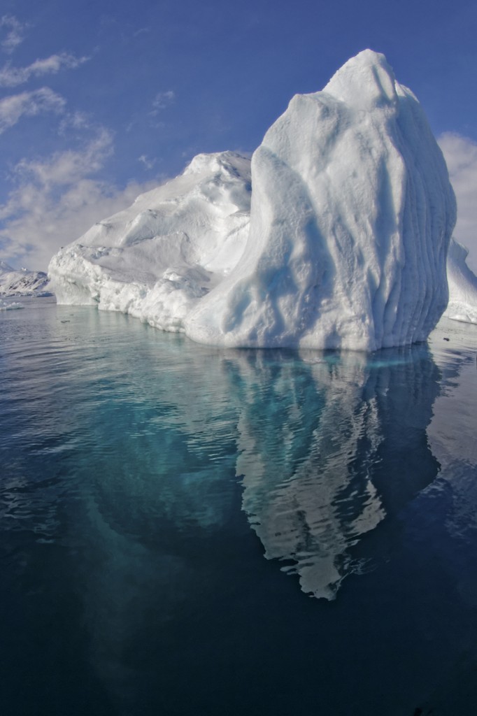 Iceberg in a fjord with a reflection on the surface and the clear visible part underwater, Tasiilaq Fjord, East-Greenland, Atlantic Ocean, Arctic. © Tobias Friedrich